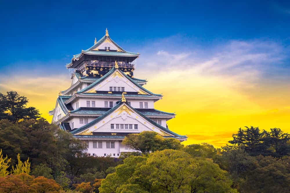 Osaka Castle with trees at the bottom and lit up by the sun in the background.